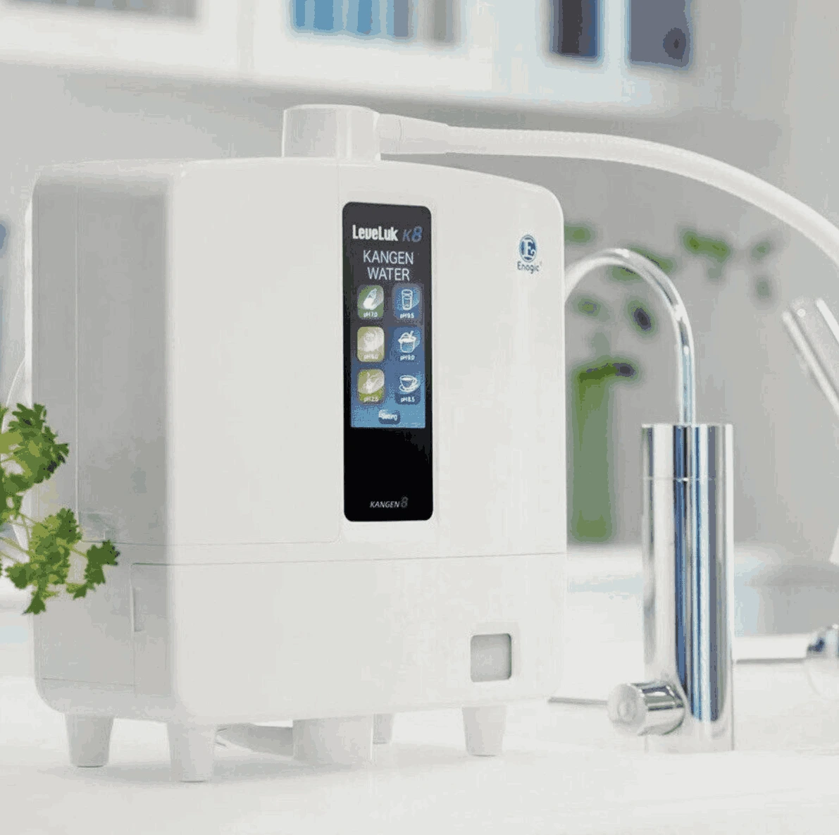 A white Kangen water ionizer machine on a kitchen counter with a silver faucet, surrounded by kitchen utensils and a plant.